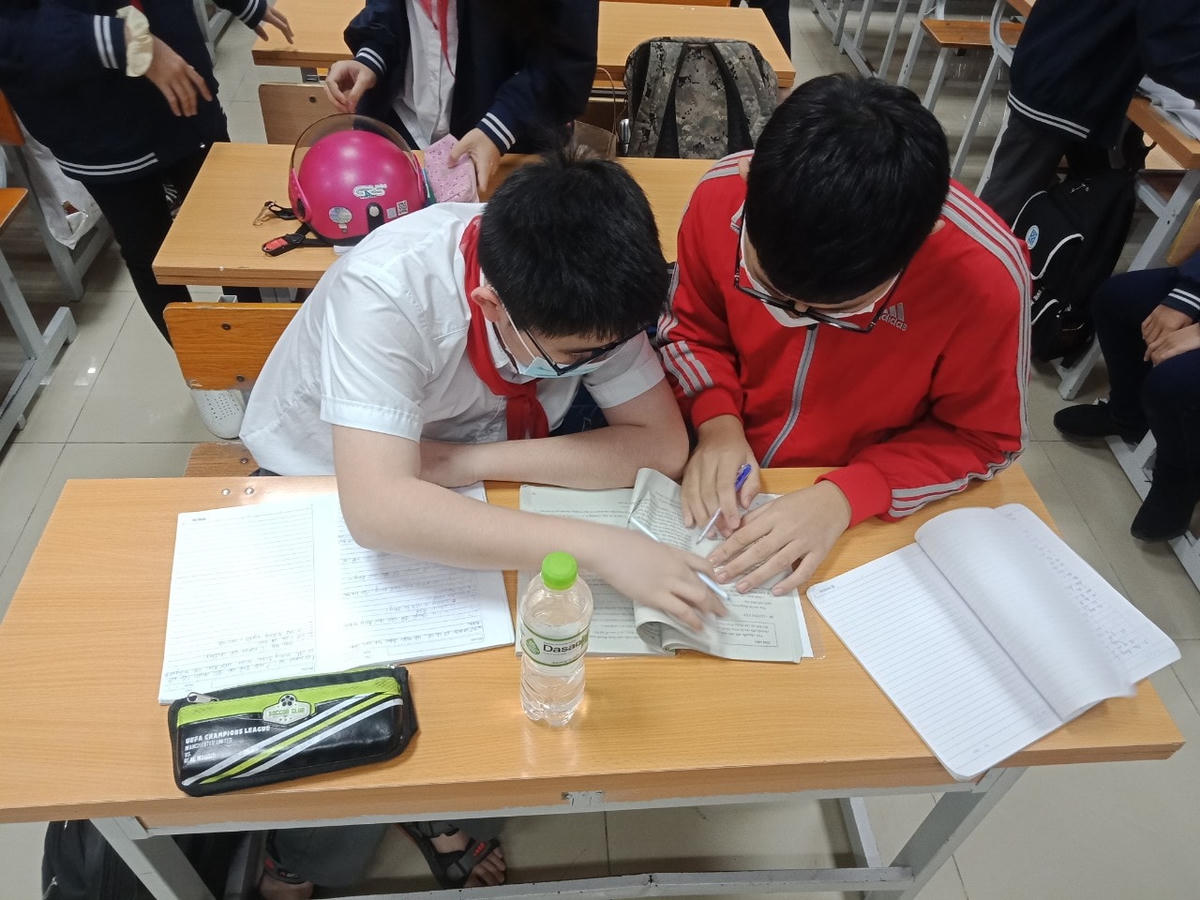Hai bạn học sinh lớp 7A1 tranh thủ trao đổi, ôn bài trước khi vào giờ học.