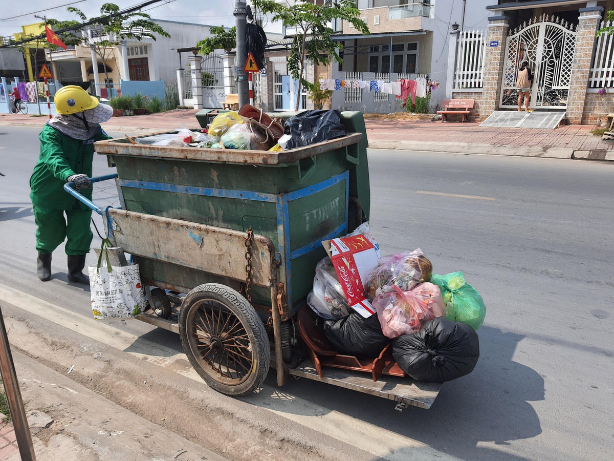 Chị công nhân Trung tâm dịch vụ đô thị nặng nhọc đẩy xe chứa đầy rác, mồ hôi ướt đẫm.