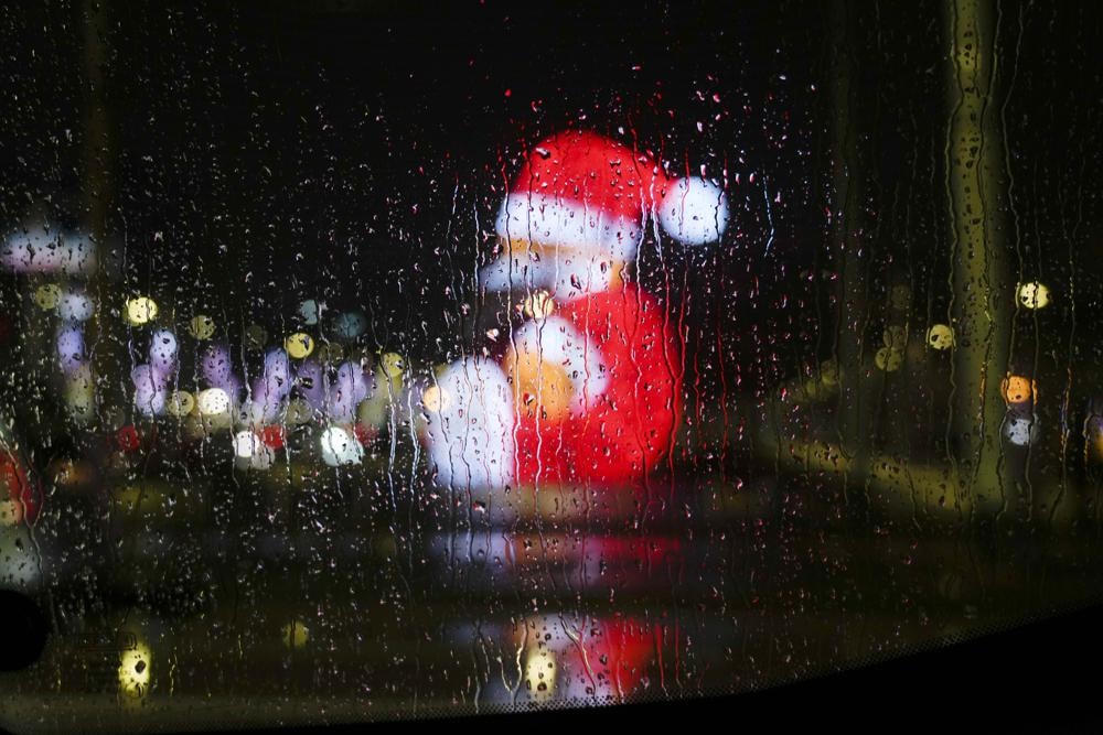 Những giọt mưa trên cửa kính ô tô, phía trước là ánh đèn thành phố và ông già Noel khổng lồ được thắp sáng ở Naples, Italy. Ảnh: AP.