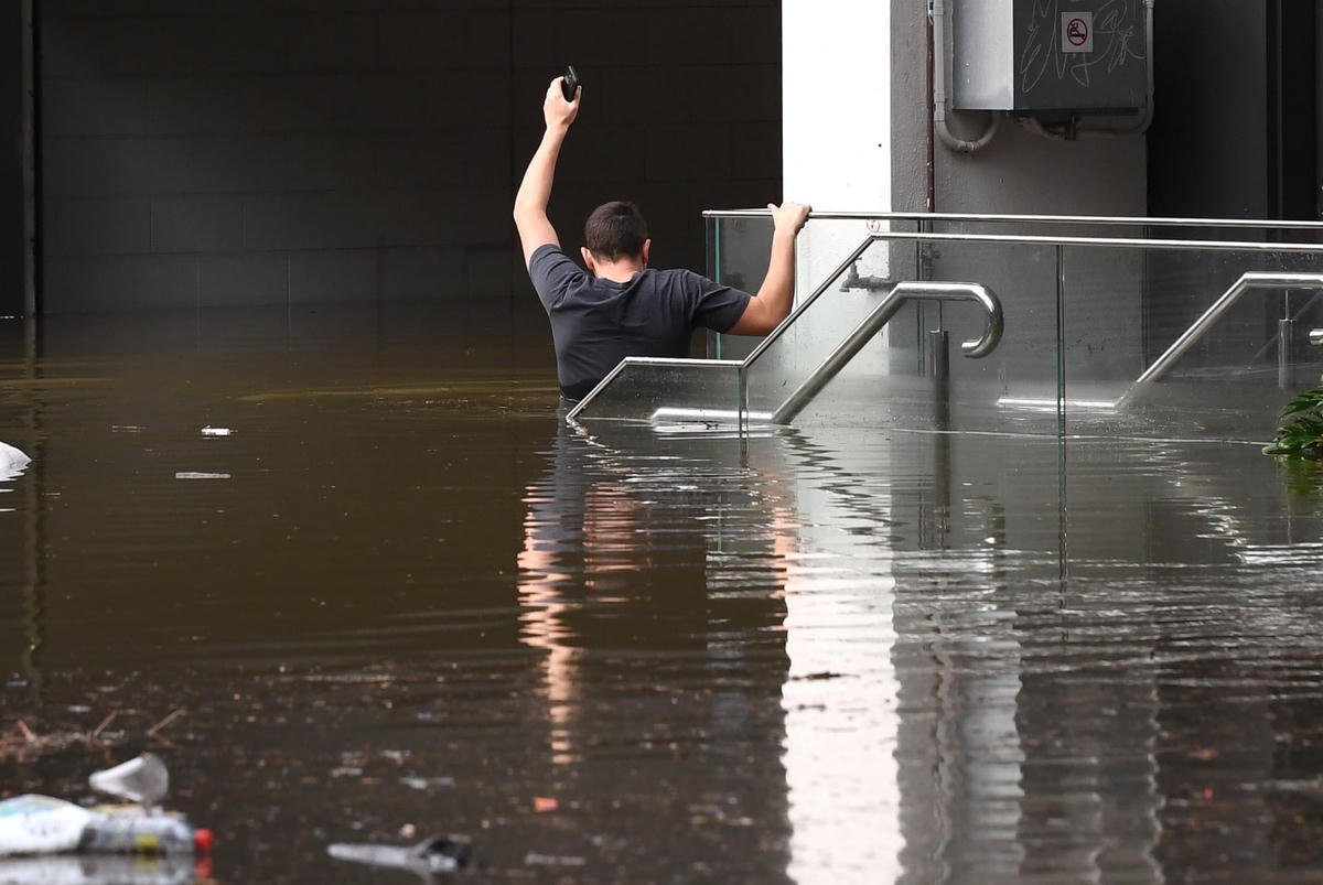Một người đàn ông khổ sở lội qua dòng nước lũ ở ngoại ô Milton ven sông Brisbane. Ảnh: Darren England / AAP.