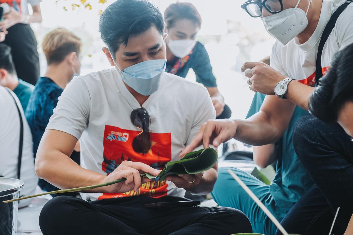 Đây là lần đầu tiên Nguyên Khang gói bánh chưng, anh được MC Quốc Bình hướng dẫn cách gập lá gói bánh.