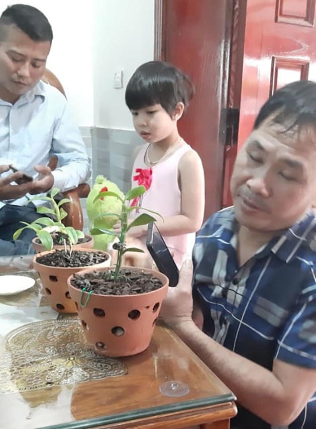 Anh Nguyễn Trọng Hán, ngồi ghế trong cùng và anh Phạm Doanh Nhân, mặc áo kẻ, cùng 3 chậu lan năm cánh trắng “rởm”. Ảnh chụp tại nhà anh Nguyễn Trọng Hán, ngày 27/2.