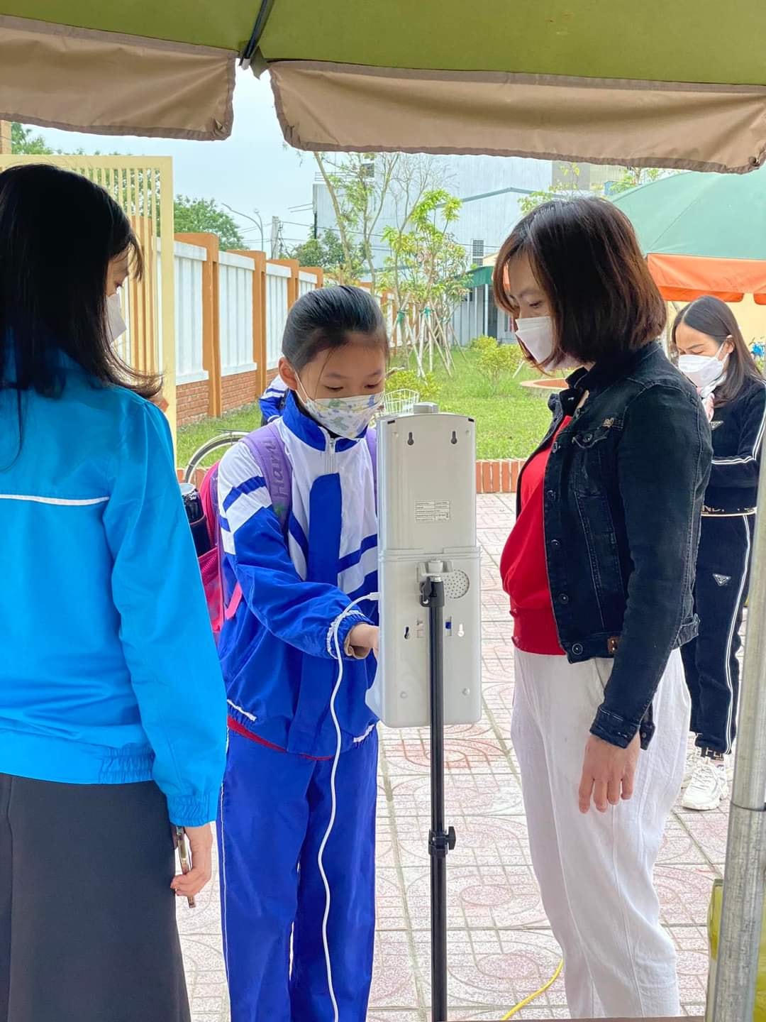 Tại Trường tiểu học Hưng Lộc 2, ngay từ cổng vào các em học sinh được hướng dẫn đến vị trí sát khuẩn tay, đo nhiệt độ trước lúc vào lớp.