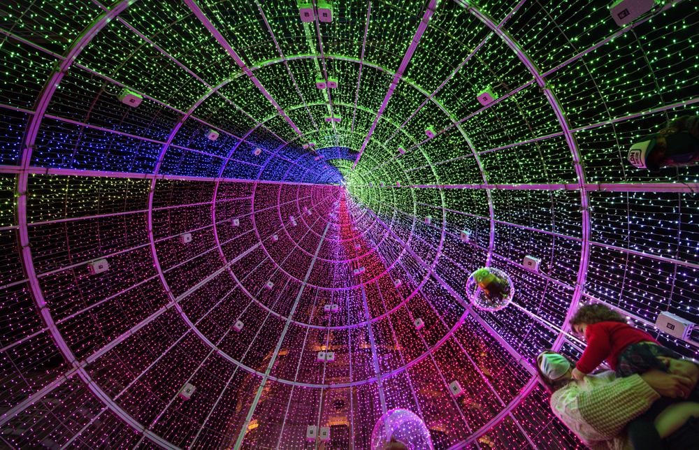 Một người phụ nữ bế đứa trẻ đứng bên trong cây thông Noel khổng lồ làm bằng đèn ở thành phố Vigo, Tây Ban Nha. Ảnh: AP.