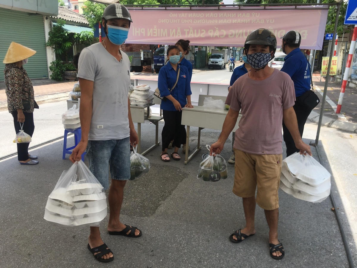 Hai người đàn ông đang cầm trên tay những suất cơm miễn phí của chương trình. 