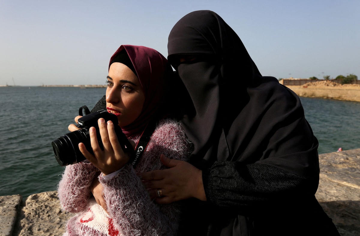 Esaraa Ismail, 22 tuổi, một nhiếp ảnh gia khiếm thị phụ thuộc vào thính giác và xúc giác để chụp ảnh, đang cùng mẹ đi tác nghiệp ở thành phố Alexandria. Ảnh: The Guardian.