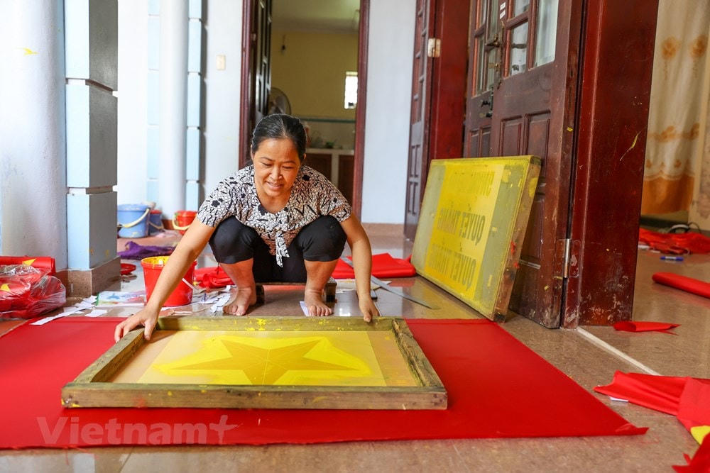 Chị Nhung năm nay 46 tuổi nhưng đã có hơn 30 năm chuyên thêu cờ Tổ quốc. Chị cho biết nhà chị đã có truyền thống may cờ 3 đời tại làng. Bố chị những năm trước phải học nghề may cờ rồi mới về truyền cho con cháu. Hơn chục năm trở lại đây, nhu cầu về cờ Tổ quốc tăng mạnh, gia đình chị trở nên tất bật hơn. (Ảnh: Minh Sơn/Vietnam+).