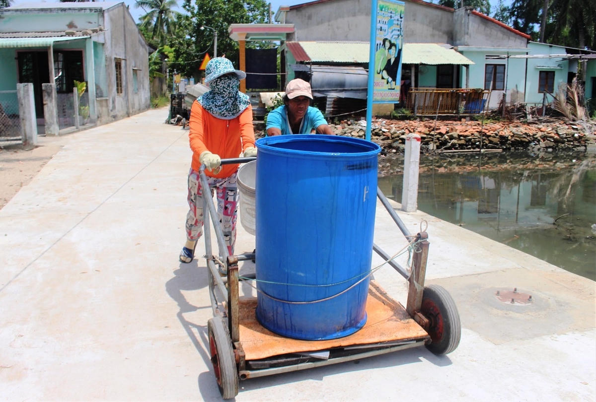 Vợ chồng ông Đồn đẩy thùng nước ngọt về nhà.