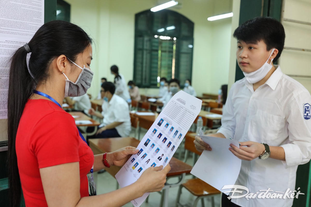 Giám thị gọi thí sinh vào phòng thi. Khi kiểm tra thẻ dự thi, các em sẽ kéo khẩu trang xuống. Sau đó, tiếp tục thực hiện đeo khẩu trang đúng quy định. Ảnh: Quang Vinh. 