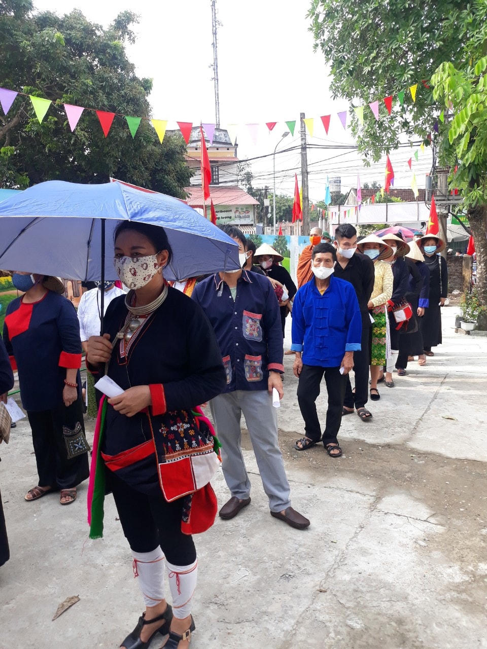 Các cử tri đang sinh hoạt hàng ngày tại Làng Văn hóa được hướng dẫn xếp hàng, giữ khoảng cách đảm bảo an toàn trước khi vào bỏ phiếu.