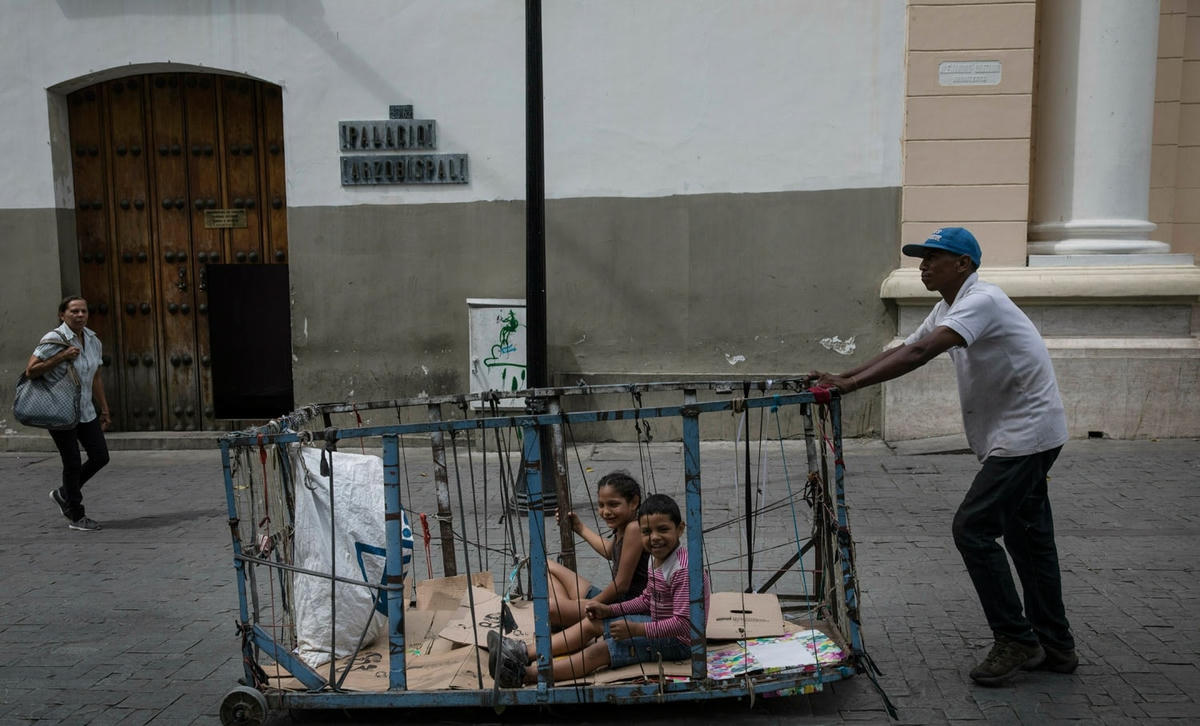 Một người đàn ông đẩy các con của mình trong xe tái chế qua trung tâm thành phố Caracas, Venezuela. Ảnh AP / Rodrigo Abd.  