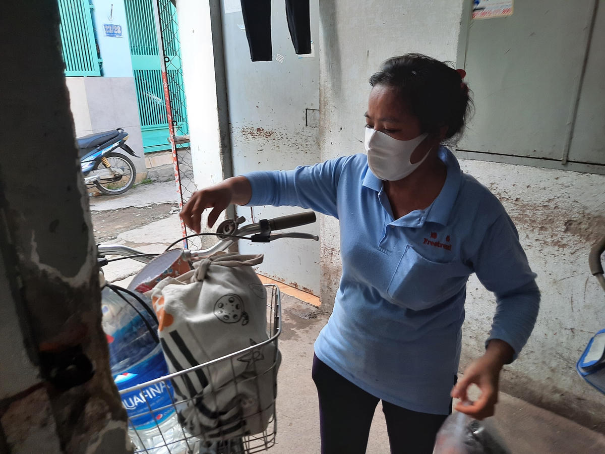 Chị Vân đi làm về, trên giỏ xe đạp có 1 bình nước 5 lít cùng bịch đồ ăn chị lấy ở công ty về.