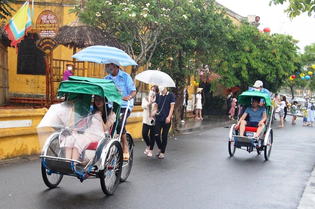 Du khách thuê xích lô tham quan phố cổ Hội An dưới trời mưa.