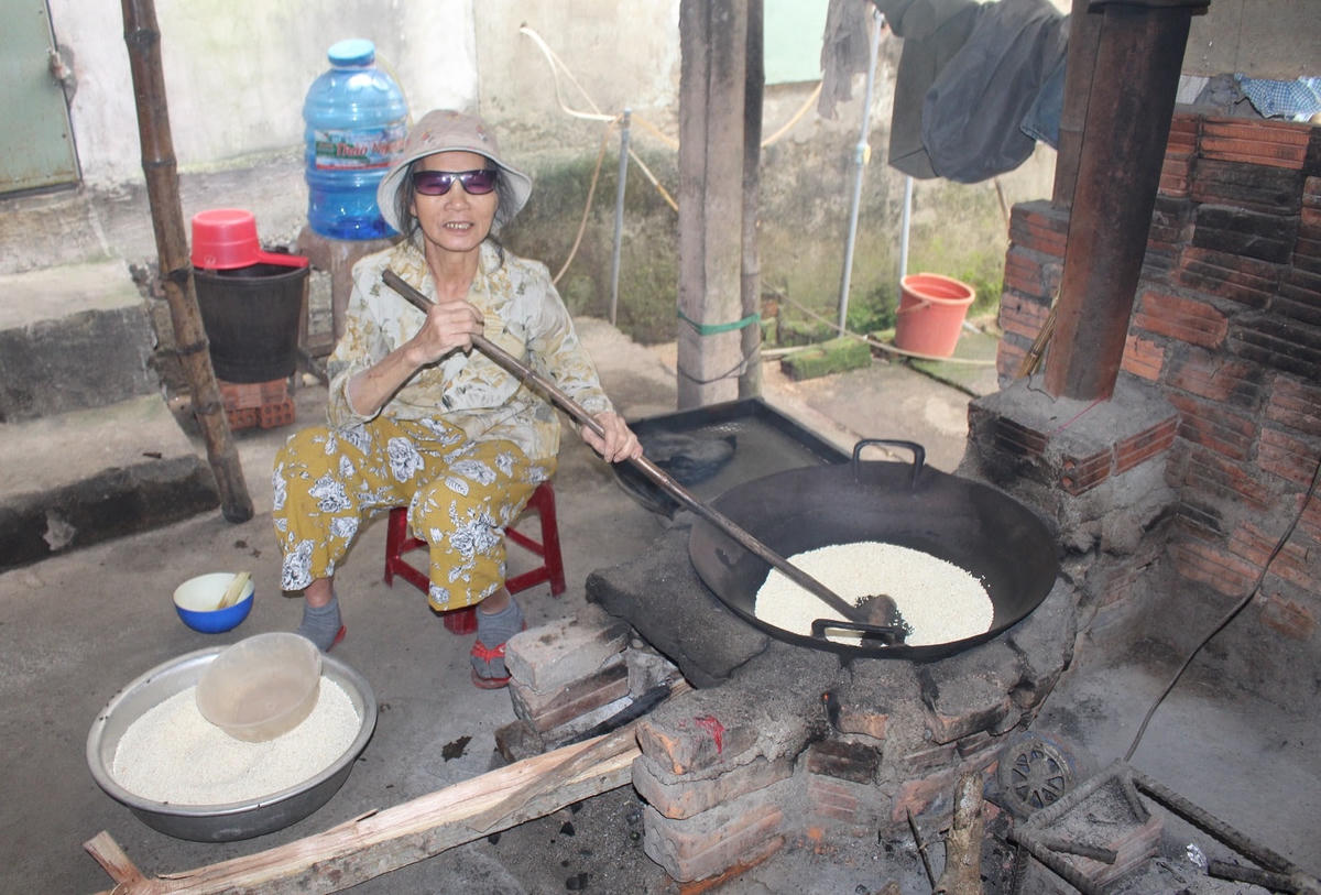 Một người thôn An Lạc đang rang nếp để làm bánh.