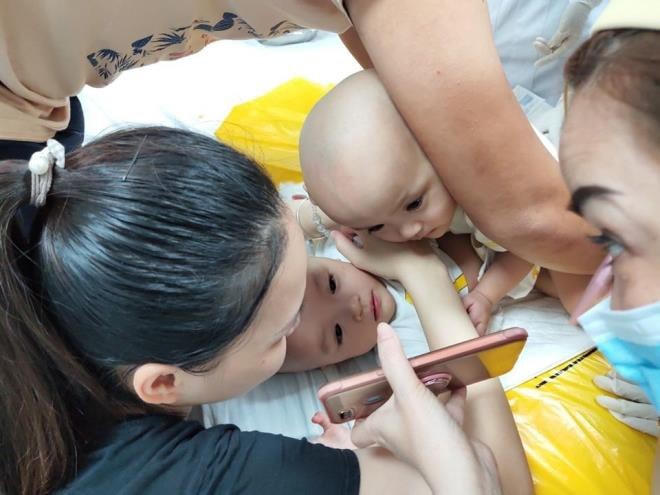 Các y tá và bố mẹ cho 2 em xem điện thoại.