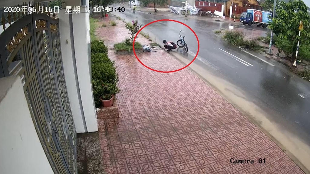 Cậu bé Phạm Trọng Đạt dừng xe đạp, moi rác ở miệng cống trên đường đi học về. (Ảnh từ clip).