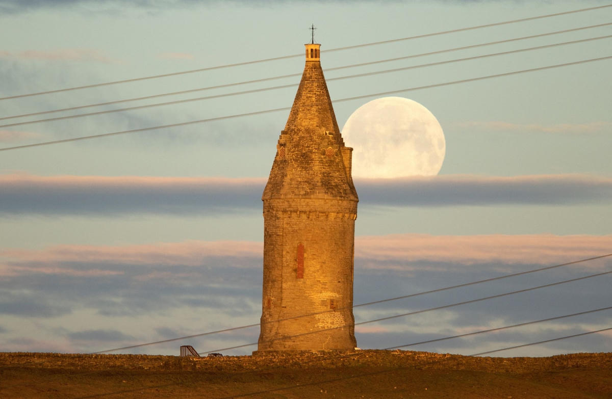 Mặt Trăng dần lặn khi trời còn chưa tối sau ngọn đồi Hartshead Pike ở Ashton-under-Lyne. Ảnh: Molly Darlington / Reuters.