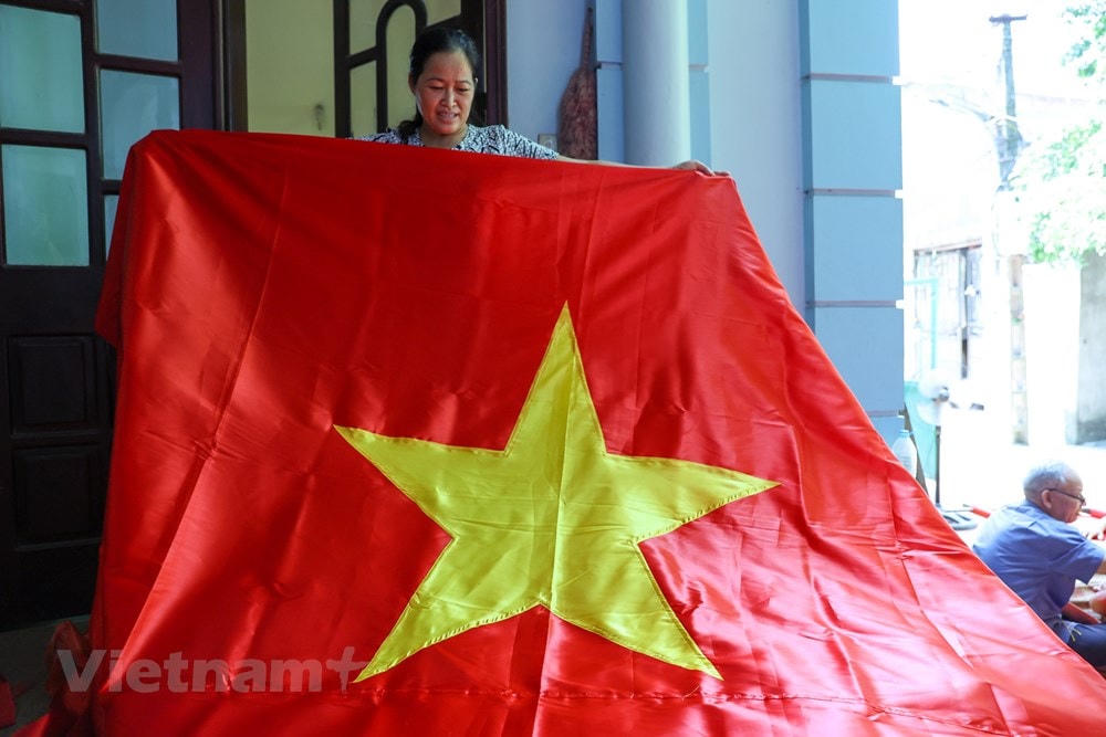 Chị Nhung cũng cho biết làm cờ may đơn giản hơn so với cờ thêu. Một ngày chị có thể làm ra hàng trăm chiếc cờ may, nhưng chiếc cờ thêu thì phải mất hàng tuần. (Ảnh: Minh Sơn/Vietnam+).