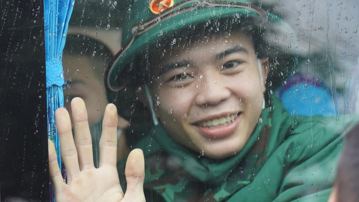 Một tân binh giơ tay chào tạm biệt người thân, quê hương để đi làm nhiệm vụ bảo vệ Tổ quốc.