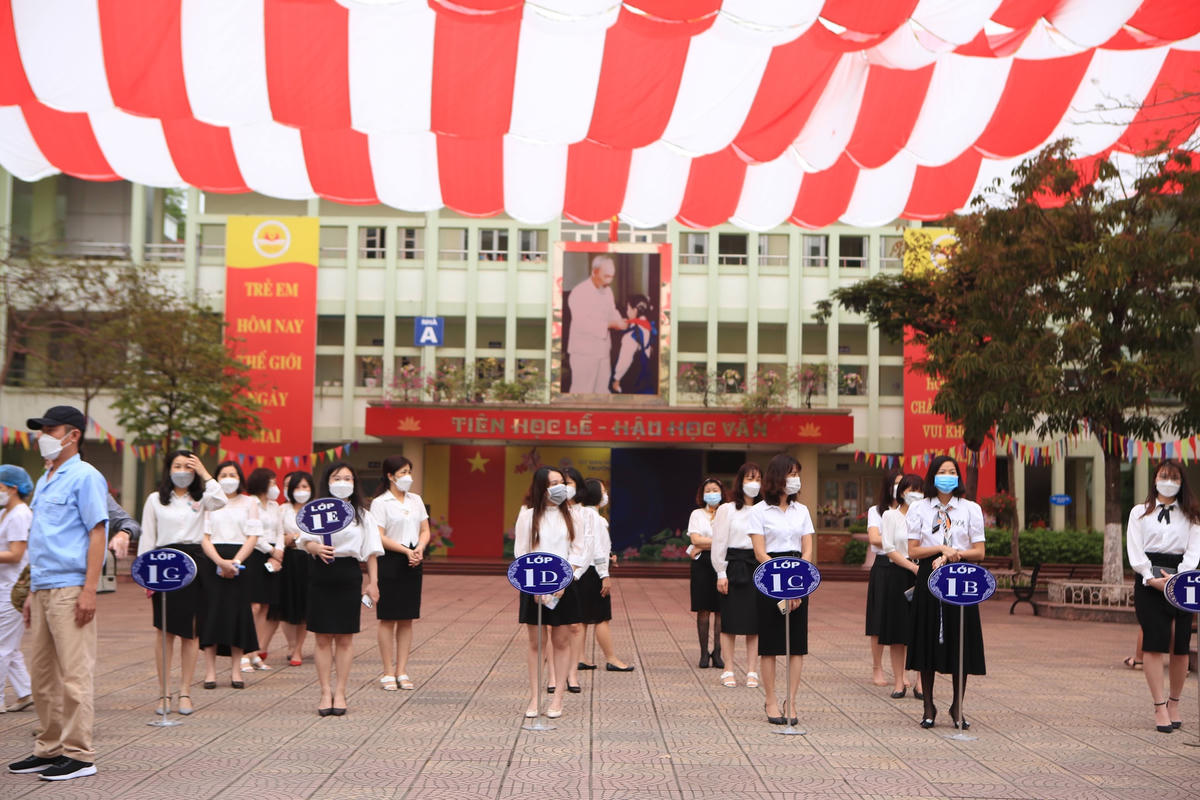 Tại các cổng trường sáng nay, nhà trường tiến hành bố trí cô giáo chủ nhiệm của khối lớp 1 ra cầm biển hiệu lớp đứng chờ học sinh ngay ở trước cổng trường.