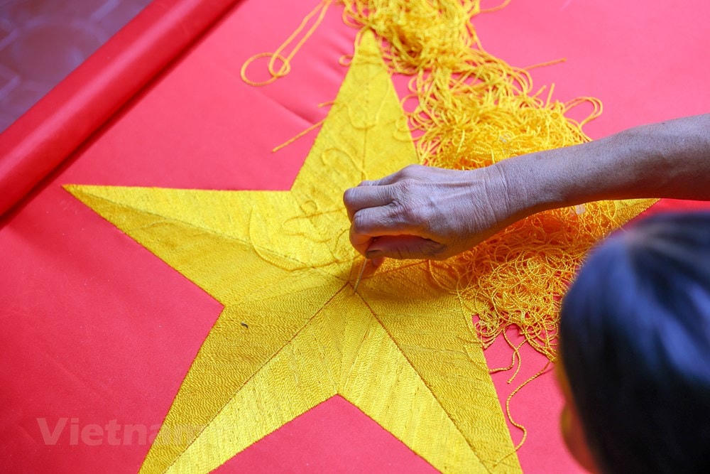 Để thêu được một lá cờ đẹp phải trải qua các công đoạn pha vải, đo, cắt, chèn sao, may… Mỗi công đoạn đều đòi hỏi người làm cờ phải thực sự khéo léo, tỷ mỉ trong từng đường kim, mũi chỉ. (Ảnh: Minh Sơn/Vietnam+).