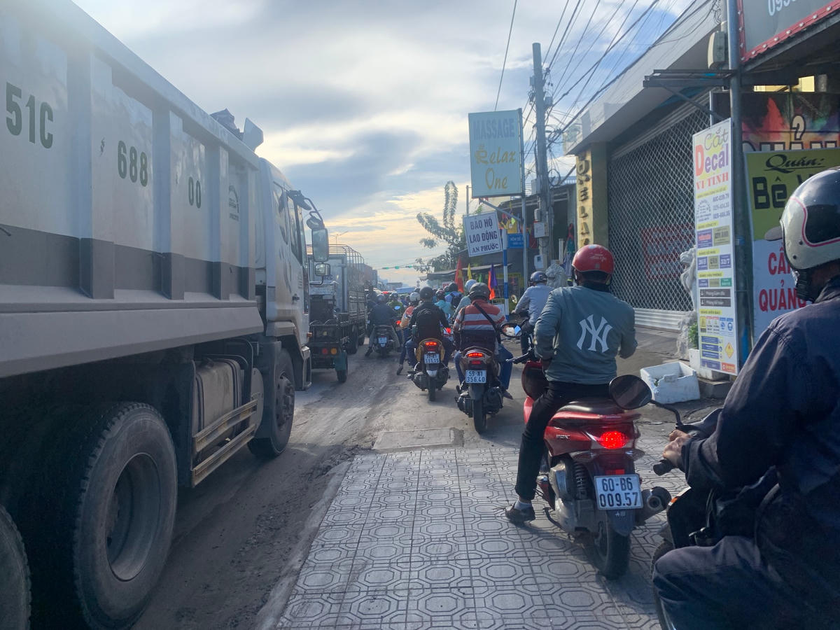 Nhiều xe ô tô tải chạy vào làn xe máy nên xe máy phải leo lề để di chuyển.