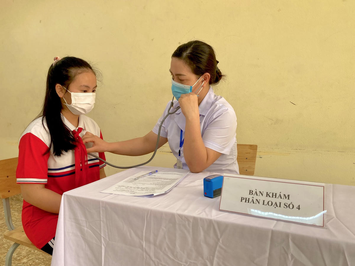 Nhân viên y tế tiến hành khám sàng lọc cho các em học sinh trước khi tiêm vaccine.