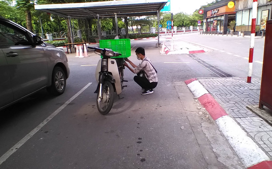 Tại lối vào bãi gửi xe, một shiper khác tự nhận là nhân viên của quầy tạp hoá quận Hoàng Mai đang chằng buộc khay hàng và đợi người mua đưa hàng xuống