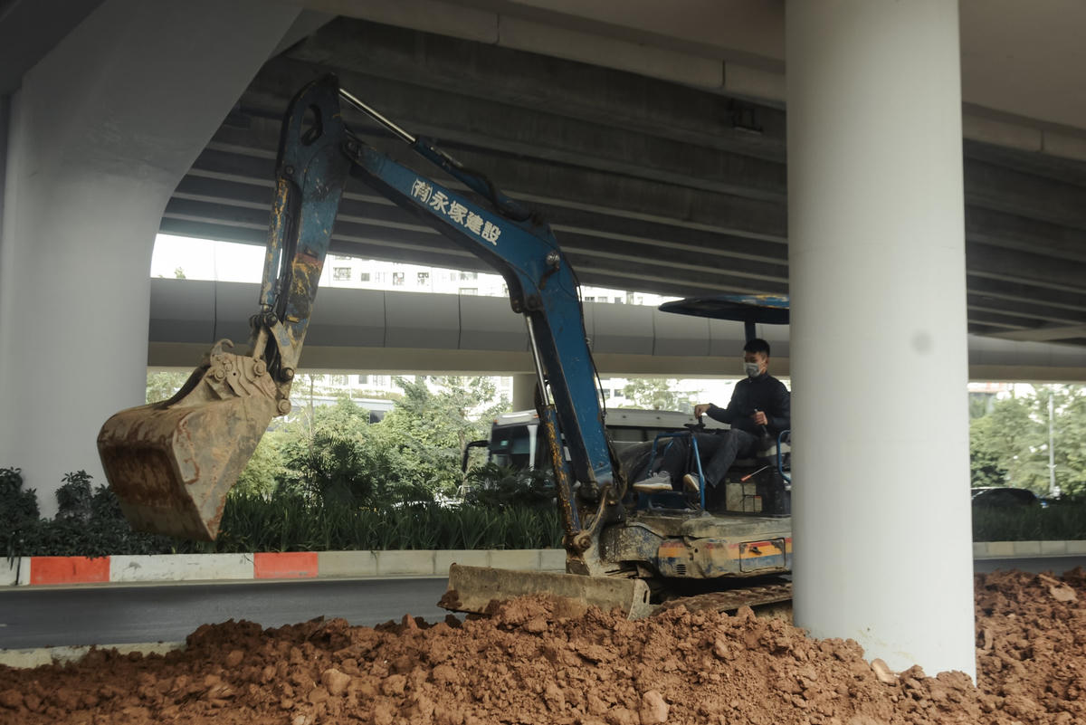 Máy xúc đang thi công san lắp đất dưới gầm nhánh lên xuống hạng mục trồng cây xanh, chỉnh trang đô thị.