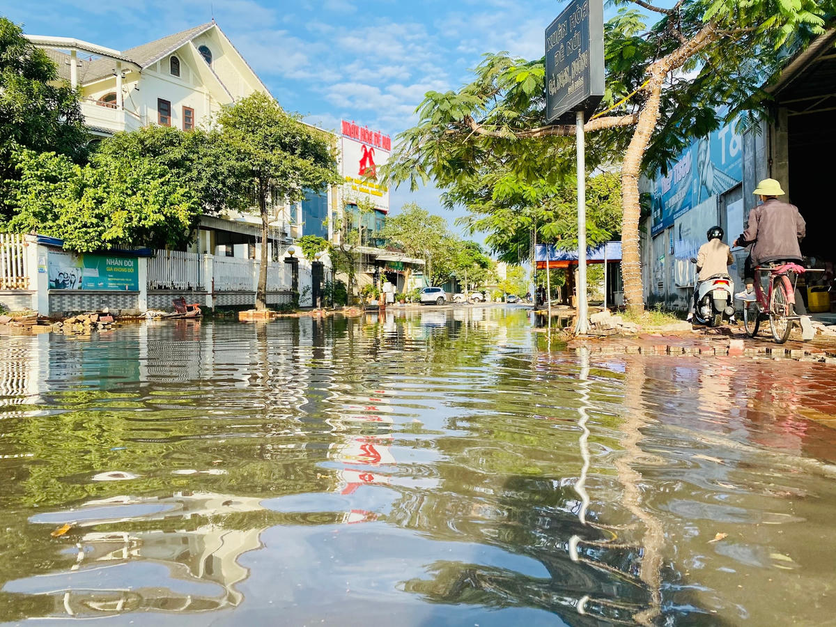 Người dân đi xe máy phải cố gắng đi men theo phần vỉa hè nhỏ hẹp chưa bị ngập nước. 