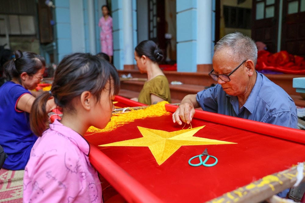 Để có thể sản xuất ra một lá cờ thêu tay, loại vải để làm cờ phải là vải sa mua từ làng La Khê (Hà Đông, Hà Nội). Vải phải dày dặn, màu đỏ tươi mới đem lại độ bền và chịu được nắng gió. Còn tua, chỉ được mua từ làng Triều Khúc (Thanh Trì, Hà Nội). (Ảnh: Minh Sơn/Vietnam+).