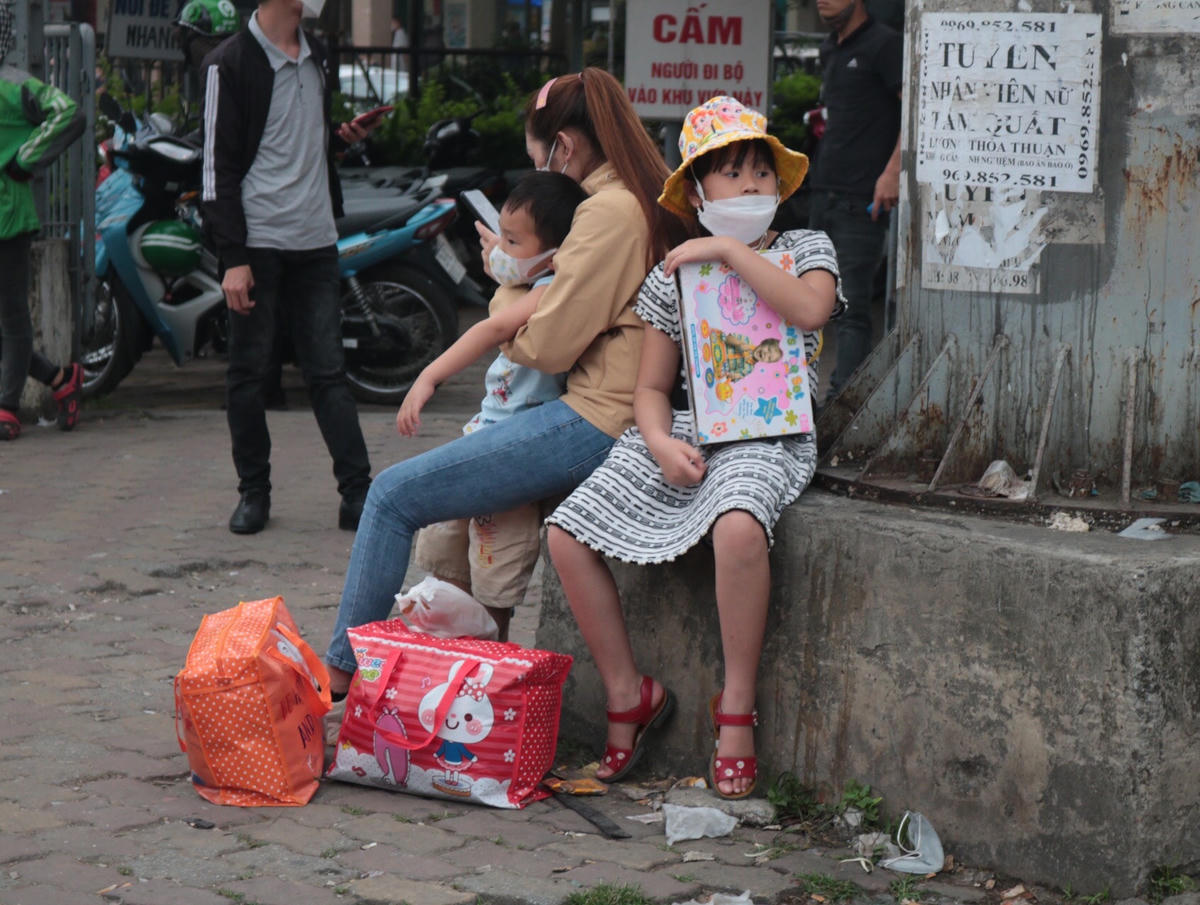 Nhiều em nhỏ vạ vật ngồi chờ xe tại bến cùng bố mẹ.