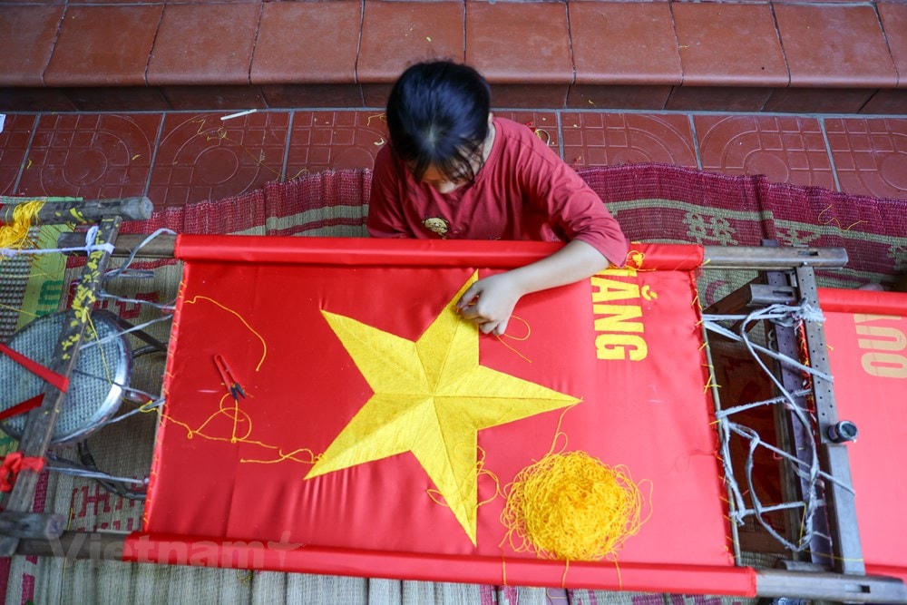 Cũng theo chị Nhung, tiền thuê nhân công thêu cờ bằng tay cũng cao hơn so với nhân công may cờ, từ 200.000 - 250.000 đồng/người/ngày. (Ảnh: Minh Sơn/Vietnam+).