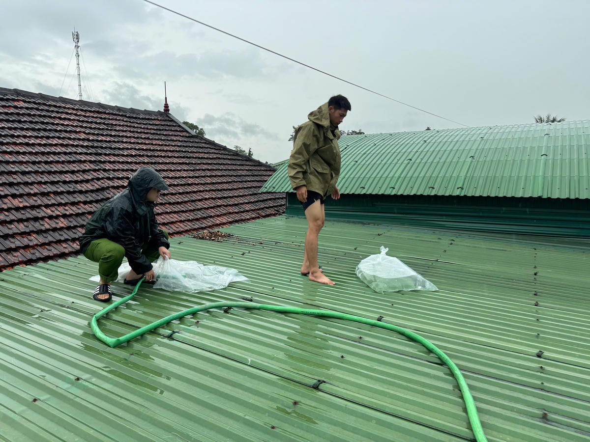 Cán bộ Công an phường Cửa Lò hỗ trợ người dân dùng bao tải nước gia cố mái tôn. Ảnh: CACC