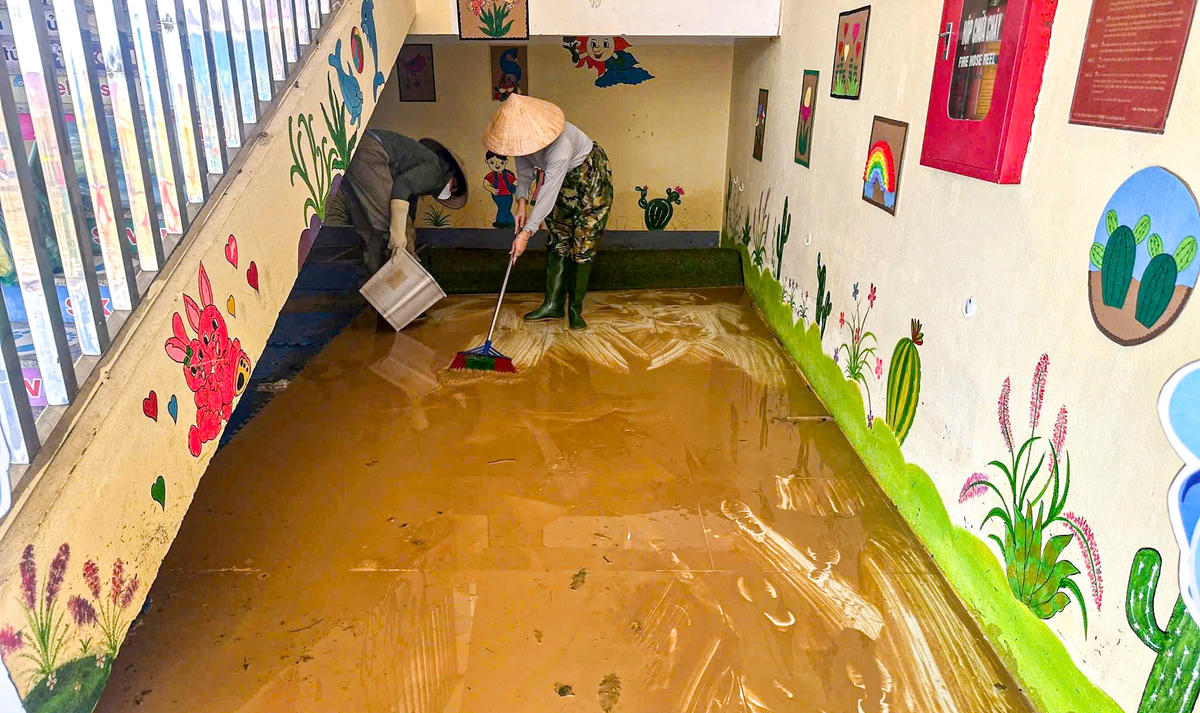 Bên trong dãy hành lang trường, giáo viên đang cọ rửa sàn nhà dính đầy bùn sau trận lũ.