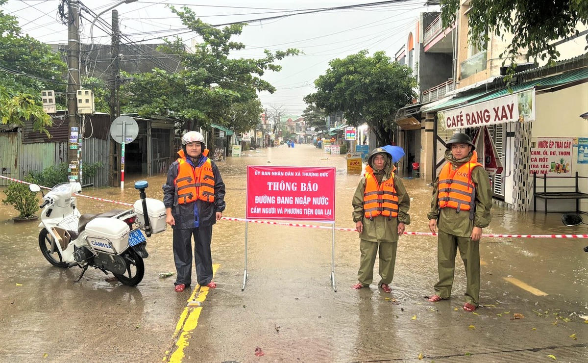 Lực lượng Công an xã Thượng Đức chốt chặn không cho phương tiện, người dân qua lại đoạn đường ngập nước. Ảnh: T. Thành.