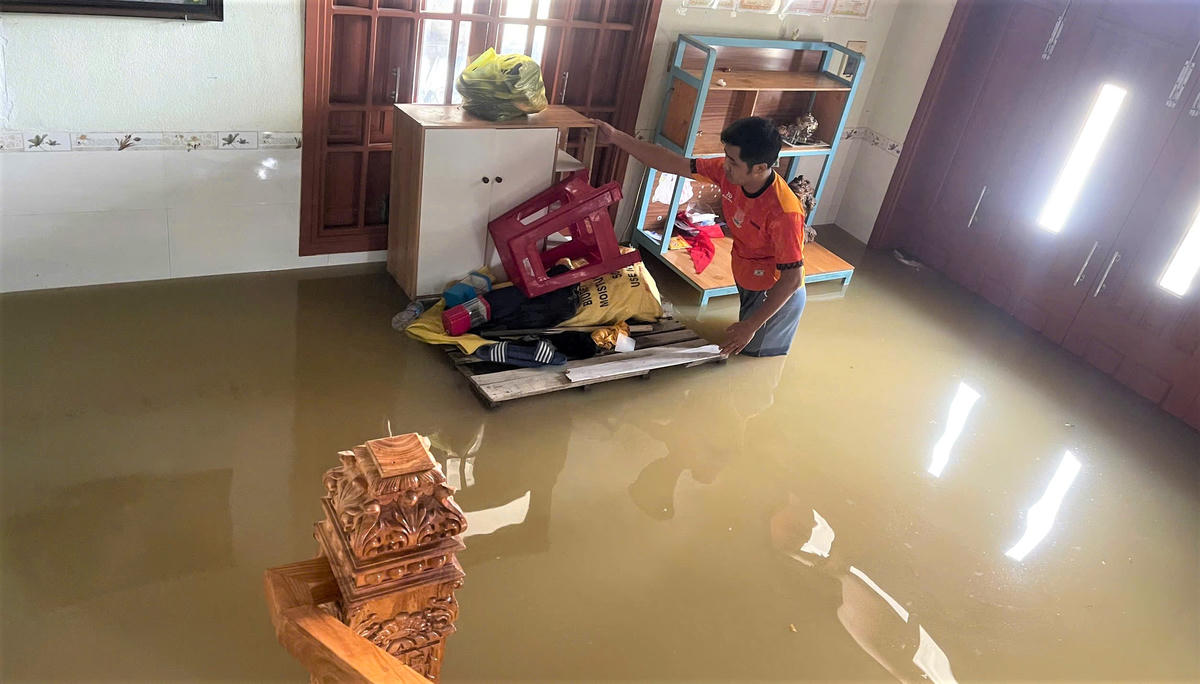 Anh Nguyễn Nhật Sang đang dọn đưa đồ đạc trong nhà ngập nước lên vị trí cao. Ảnh: Tấn Thành.