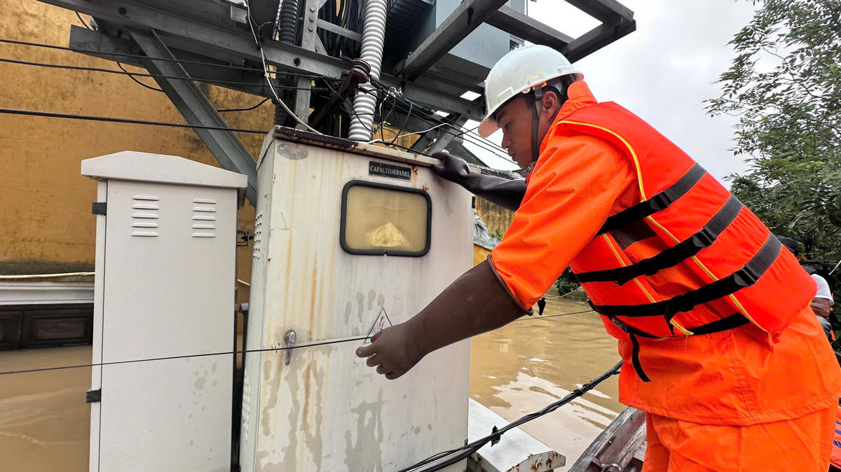 Công nhân Đội Quản lý điện Hội An (Công ty Điện lực Đà Nẵng) kiểm tra lưới điện khu vực ngập lụt. Ảnh: Quang Khải.