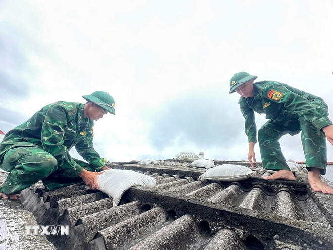 Các chiến sỹ giúp người dân đưa bao cát lên mái nhà để tránh tốc mái tôn khi gió bão. (Ảnh: TTXVN phát)