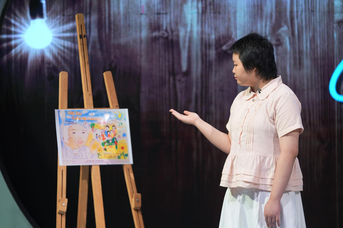 Chu Ánh Tuyết giới thiệu về một tác phẩm của mình. Chính những gam màu tươi sáng trong tranh đã giúp em quên đi kim tiêm, truyền dịch và nỗi đau bệnh tật. Ảnh: VTV