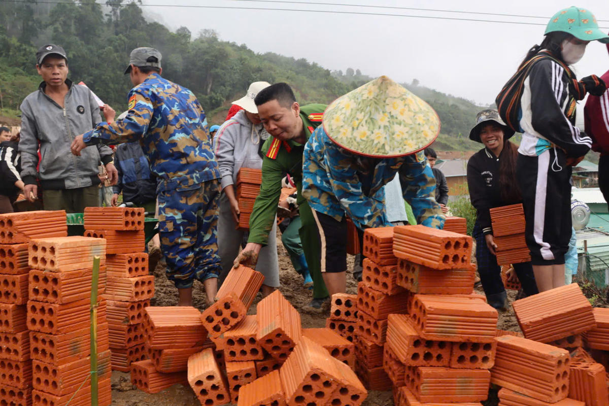 Lực lượng chức năng xã Măng Ri cùng người dân vận chuyển gạch để xây dựng nhà mới. Ảnh: CV.