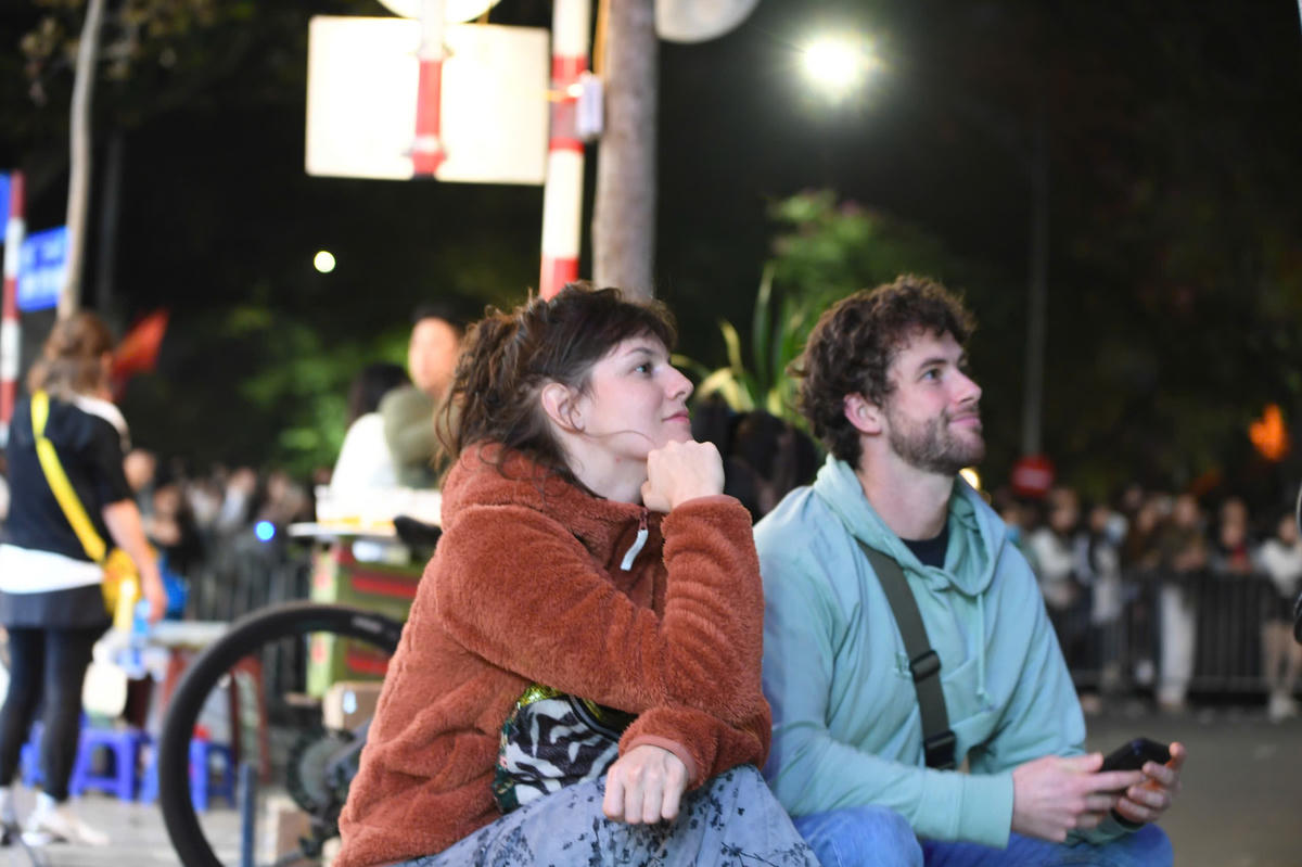 Hai vị khách quốc tế chọn một góc riêng, thưởng thức bữa tiệc âm nhạc qua màn hình lớn tại hồ Gươm. Ảnh: Phạm Sỹ.