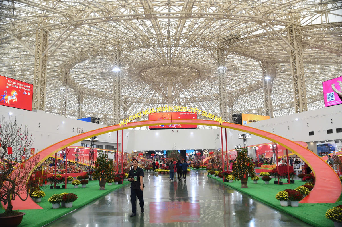 Không gian Hội chợ Mùa Xuân 2026 rực rỡ sắc xuân với hệ thống gian hàng trải dài, cờ hoa và tiểu cảnh trang trí đậm chất truyền thống, tạo nên điểm hẹn văn hóa – thương mại sôi động giữa dòng người tham quan tấp nập. Ảnh: Phạm Sỹ.