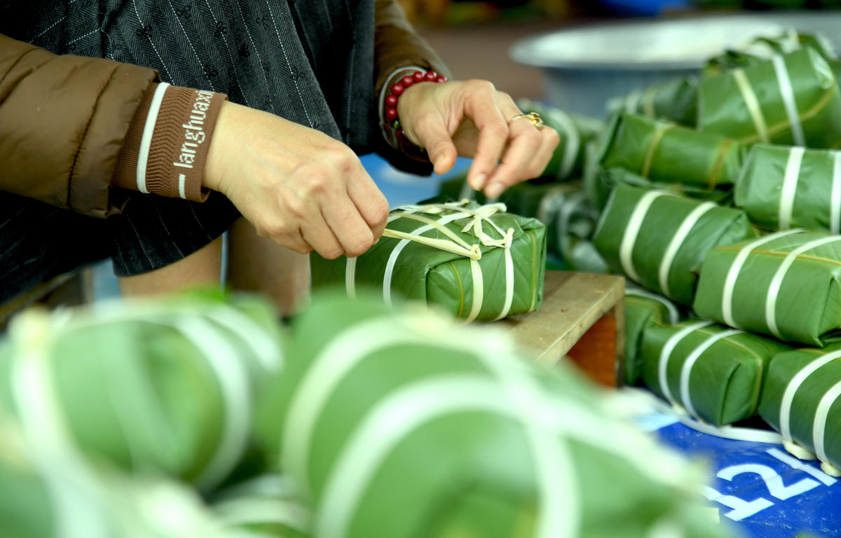 Đôi bàn tay thoăn thoắt, nhịp nhàng gấp từng nếp lá, dẻo mềm sợi lạt, tạo lên một chiếc bánh chưng vuông vắn và đầy đặn. Trăm chiếc như một. Ảnh: Phạm Sỹ.. 