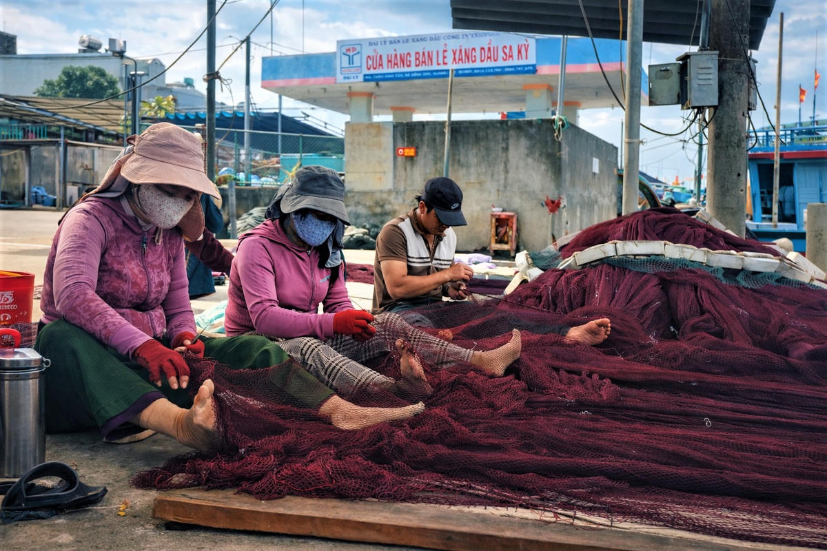 Nhân công, ngư dân đang ngồi vá lưới cho tàu thuyền chuẩn bị vươn khơi. Ảnh: Nguyễn Tín