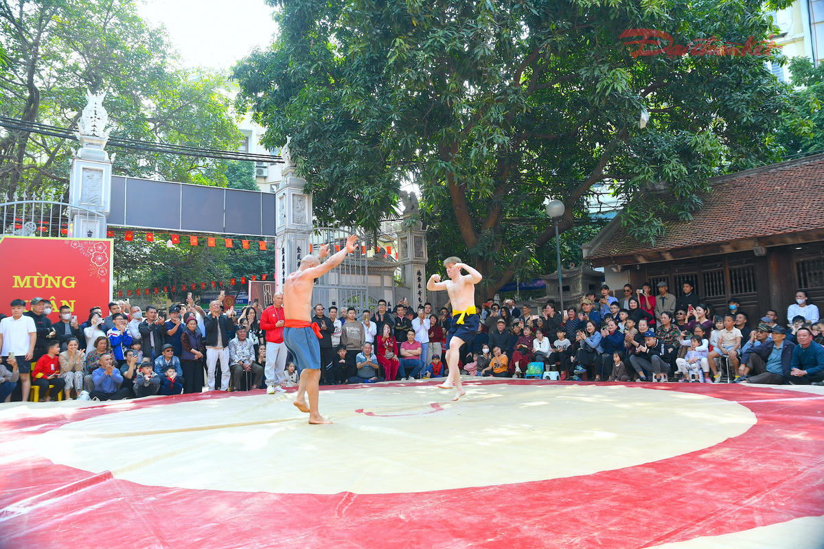 Trên nền cờ hội rực sắc, những màn so tài quyết liệt góp phần làm nên khí thế tưng bừng của lễ hội vật Mai Động. Không chỉ sôi động với đô vật trong nước, sới vật Mai Động còn chào đón sự góp mặt của các đô vật quốc tế, làm tăng thêm sức nóng cho từng trận đấu. Ảnh: Phạm Sỹ.