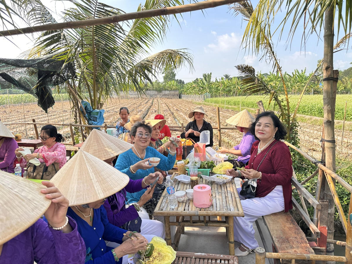 Du khách thích thú thưởng thức món bánh xèo miền Tây dân dã tại chợ phiên Xóm Rẫy, giữa không gian đồng ruộng thoáng đãng ở Đồng Tháp. (Ảnh: Trung Ngãi).