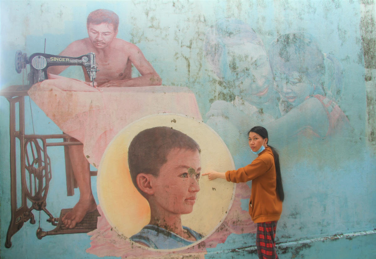 Chị Lương Thị Tường Vy chỉ bức tranh vẽ gia đình mình bị phai mờ. Ảnh: Tấn Thành.