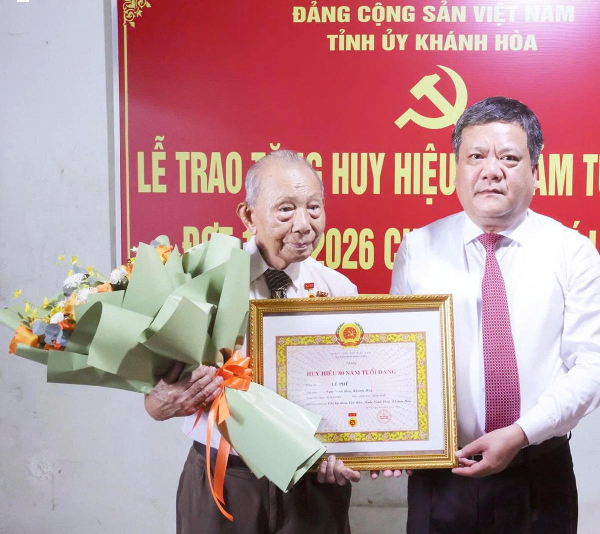 Ông Trần Phong, Bí thư Tỉnh ủy Khánh Hòa trao Huy hiệu 80 năm tuổi Đảng và tặng hoa chúc mừng đảng viên Lê Phê.