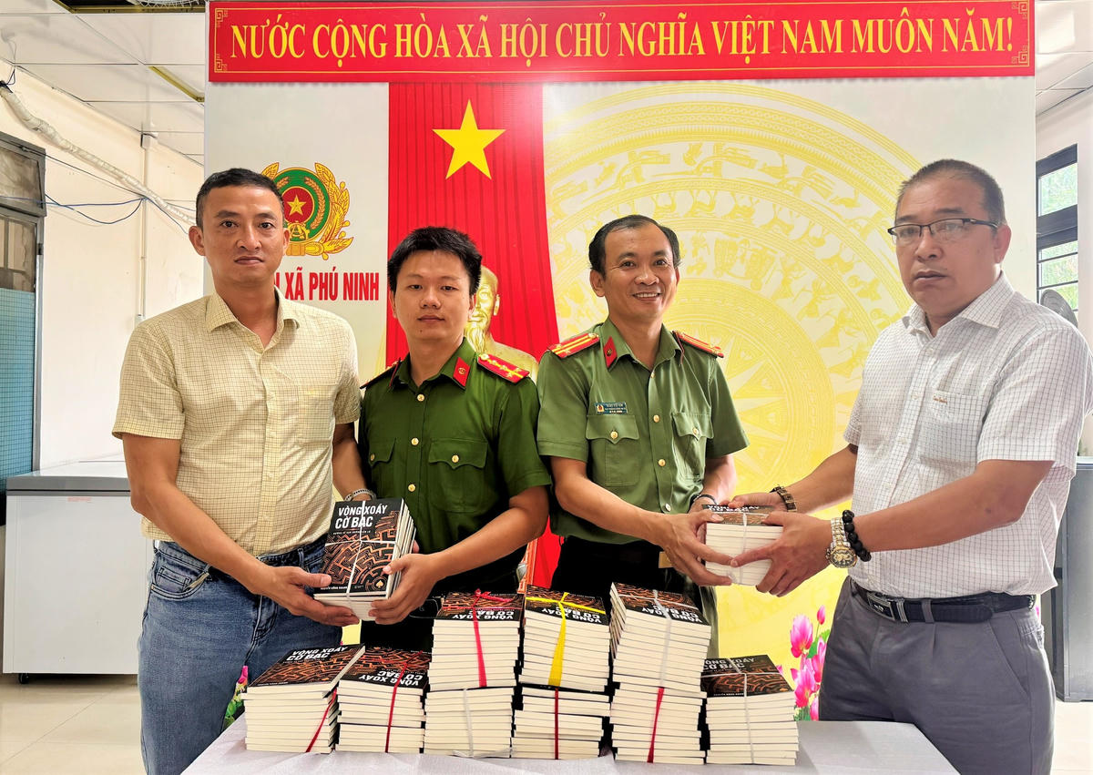 Nhà báo Đinh Tấn Thành, (bên phải) Phụ trách Văn phòng đại diện báo Đại đoàn kết tại khu vực miền Trung trao tặng cuốn sách “Vòng xoáy cờ bạc - Đường về sau những lầm lỡ" cho Công an xã Phú Ninh. Ảnh: CĐ.